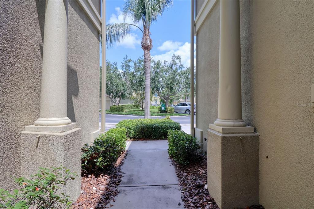 A concrete walkway leads between two columns toward a street with trees and a car — 6622 83RD AVENUE N, PINELLAS PARK, FL