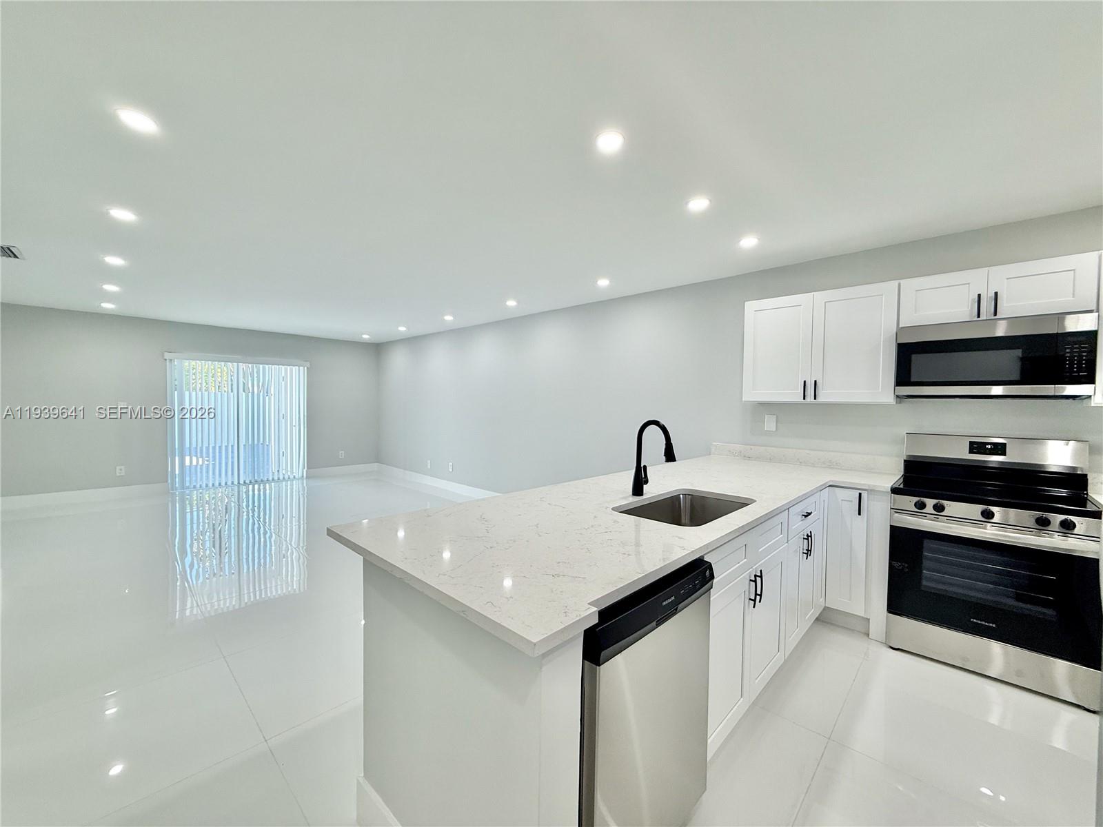 A modern kitchen with white cabinets, stainless steel appliances, and quartz countertops overlooks an open-concept living area — 11240 SW 33rd Cir Pl, Miami FL 33165, MIAMI, FL