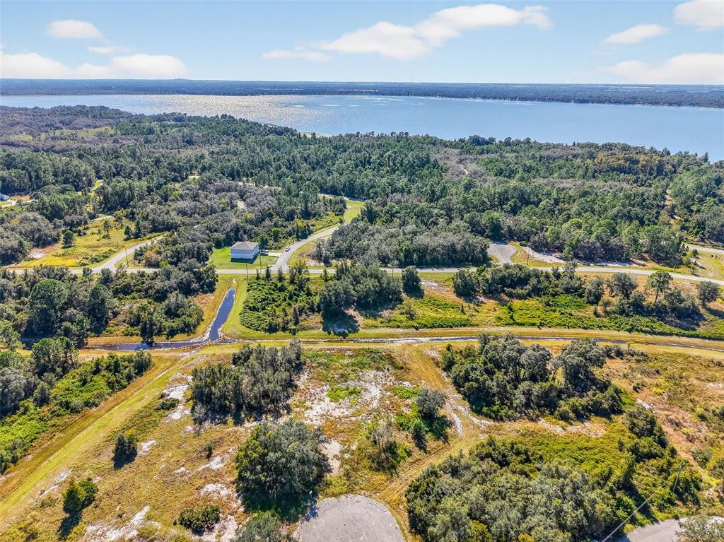 An aerial view shows a vacant, grassy lot with trees near a road and lake — 1417 SEBRING WAY, POINCIANA, FL