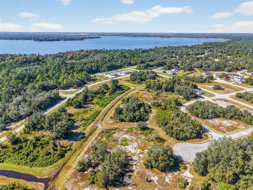 An aerial view shows a wooded residential area with dirt roads near a large lake — 1417 SEBRING WAY, POINCIANA, FL