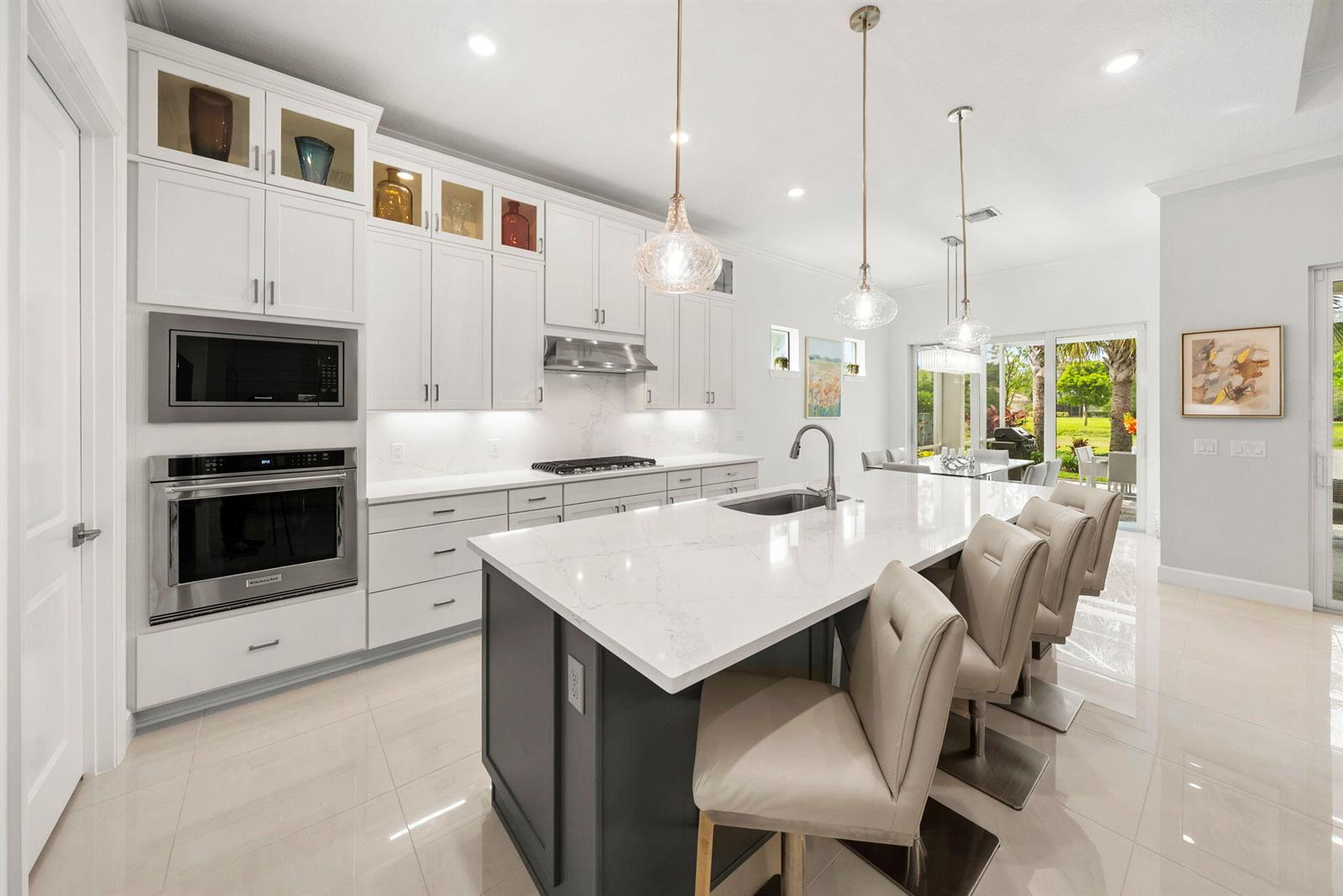 A modern kitchen features white cabinetry, a dark gray island, and stainless steel appliances — 4588 Matilda Court, Delray Beach FL 33445, DELRAY BEACH, FL