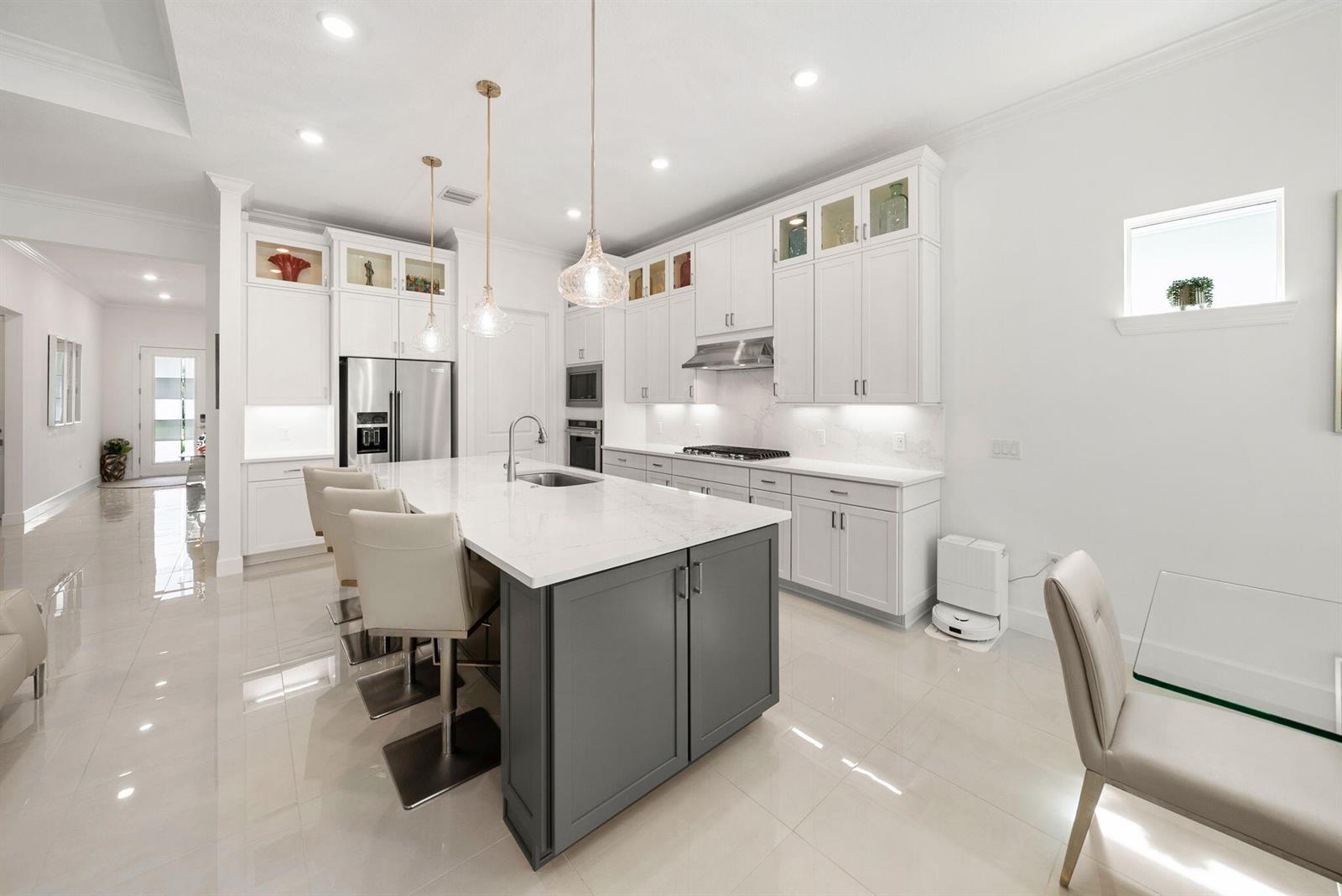 A modern kitchen features white cabinetry, a gray island with bar seating, and tile flooring — 4588 Matilda Court, Delray Beach FL 33445, DELRAY BEACH, FL