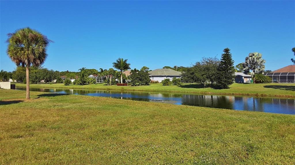 A grassy lawn slopes down to a canal with houses and palm trees in the background — 847 ROTONDA CIRCLE, ROTONDA WEST, FL