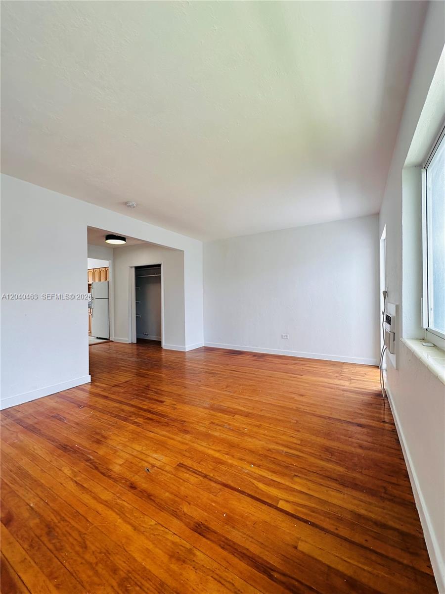 An empty room features hardwood floors, white walls, and a doorway leading to a kitchen — 2045 Calais Dr # 7, Miami Beach FL 33141, MIAMI BEACH, FL