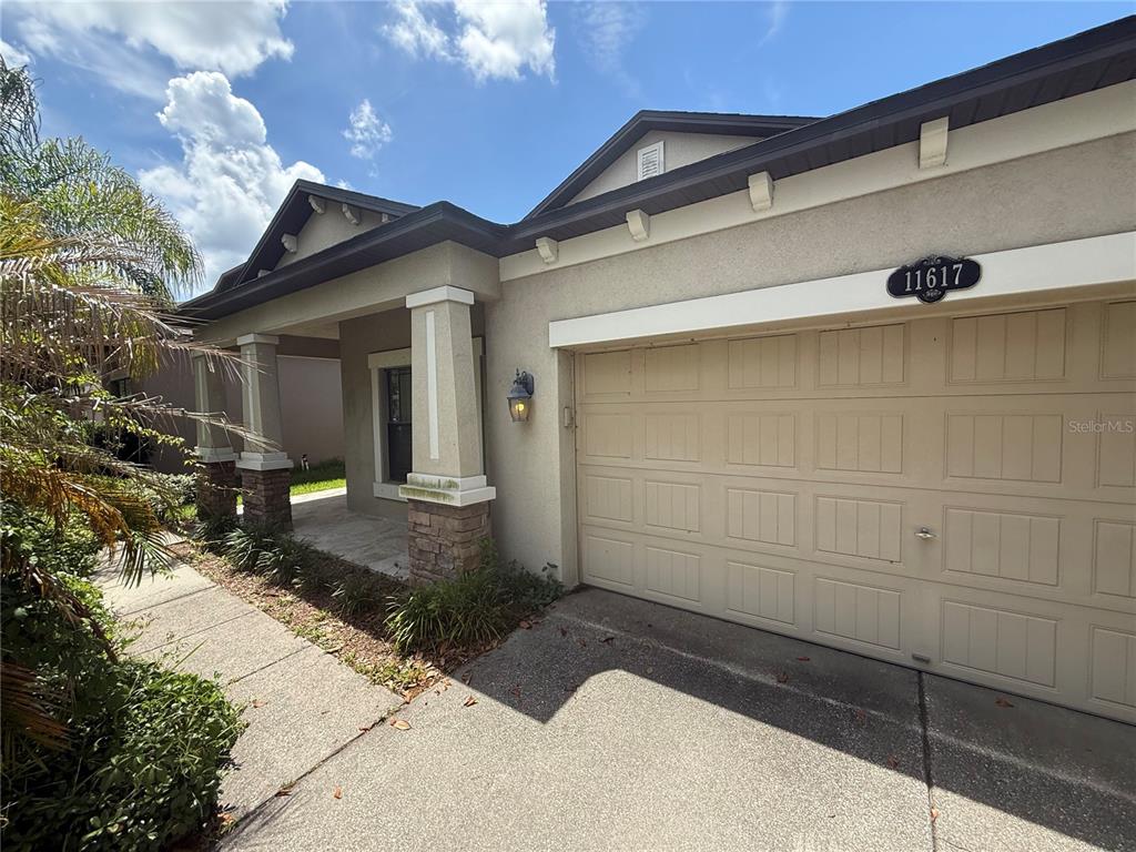 The exterior of a single-story house features a tan stucco facade, a garage, and a porch — 11617 PALMETTO PINE STREET, RIVERVIEW, FL