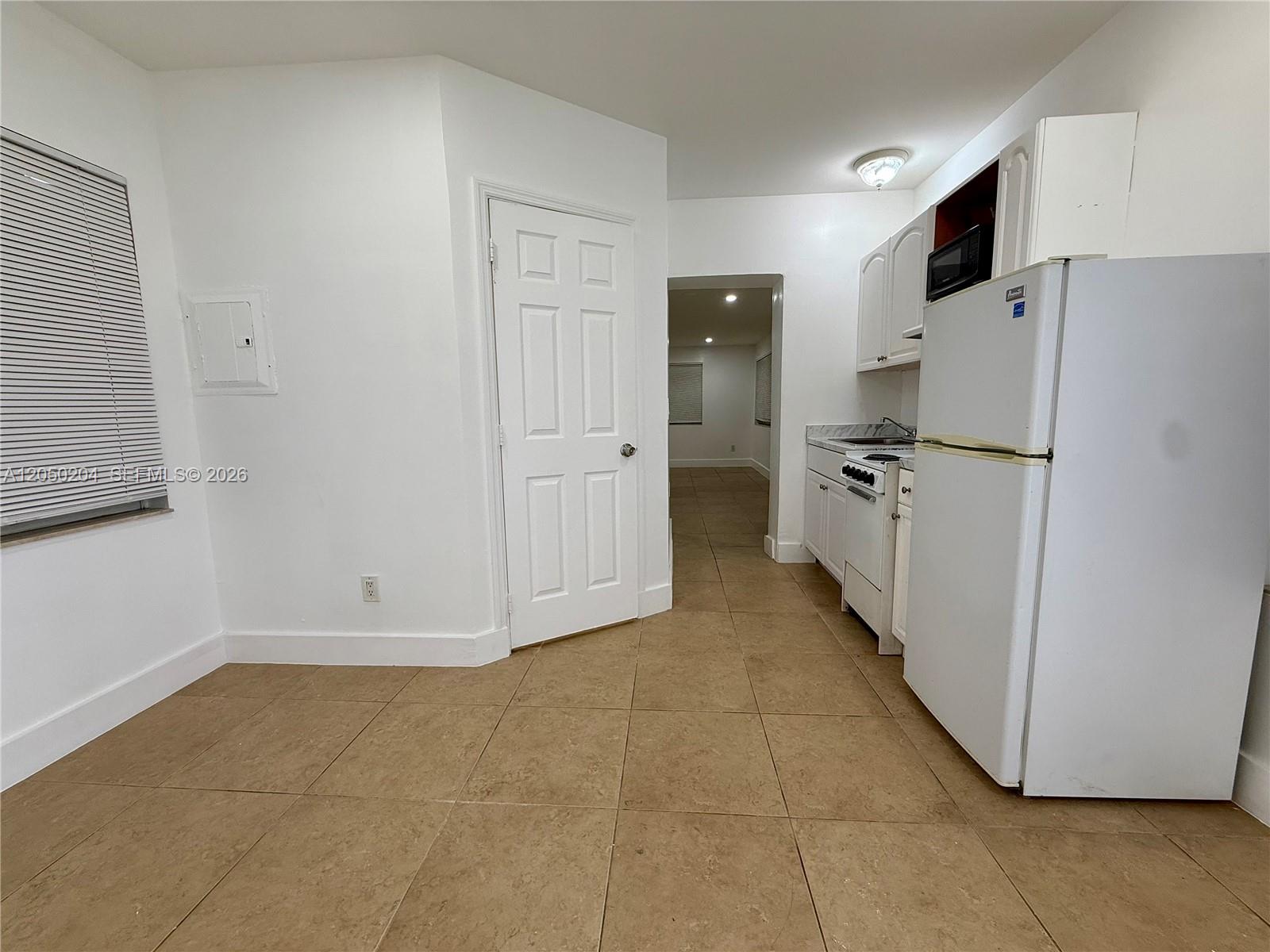 A kitchen with white cabinets, a white refrigerator, and tan tile flooring — 427 NE 62nd St # 14, Miami FL 33138, MIAMI, FL