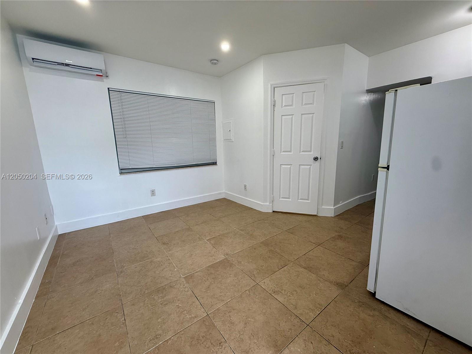 A room with white walls, tiled flooring, a window with blinds, and a wall-mounted AC unit — 427 NE 62nd St # 14, Miami FL 33138, MIAMI, FL