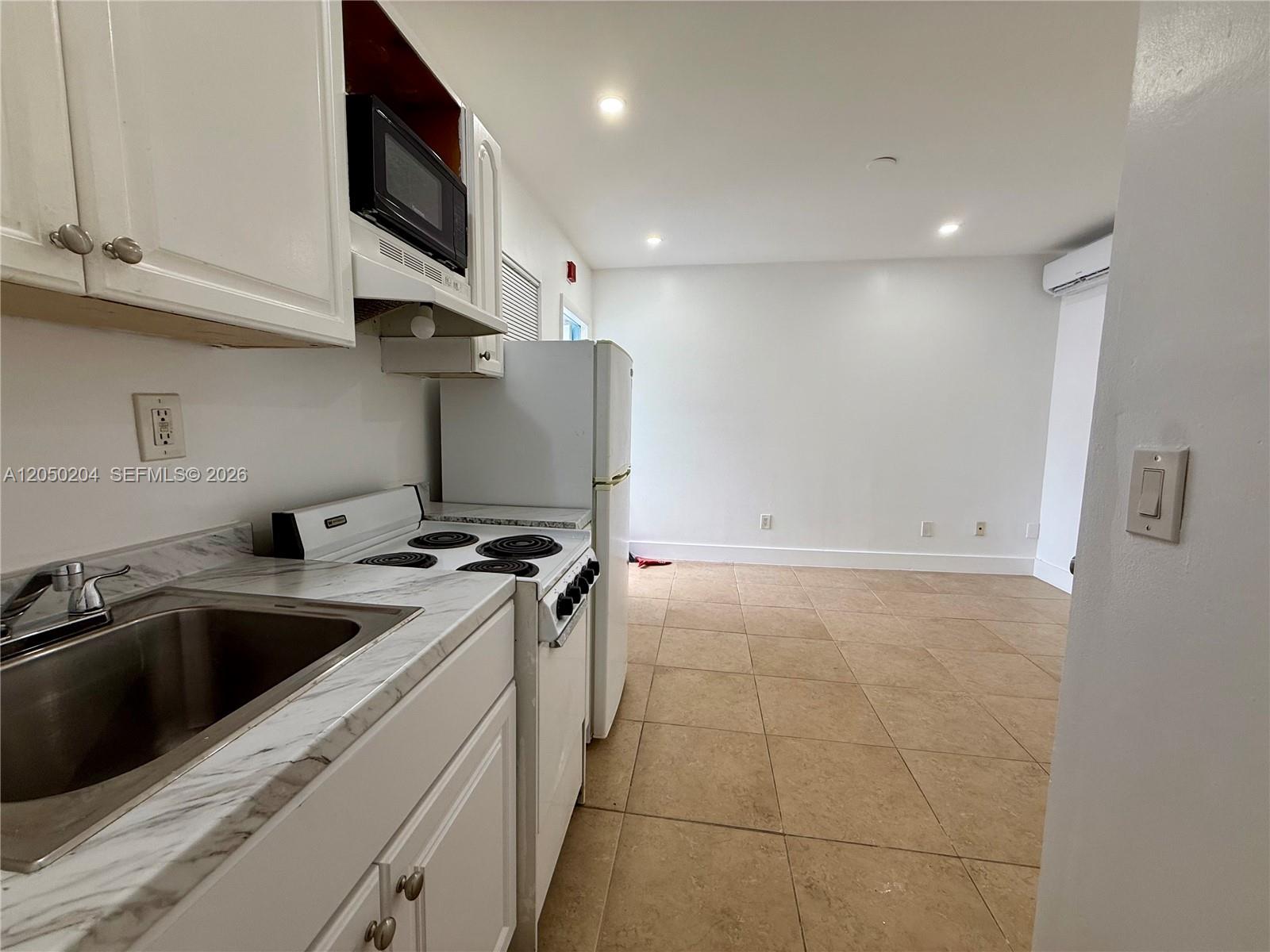 A kitchen with white cabinets, a white stove, and a refrigerator opens to a tiled room — 427 NE 62nd St # 14, Miami FL 33138, MIAMI, FL