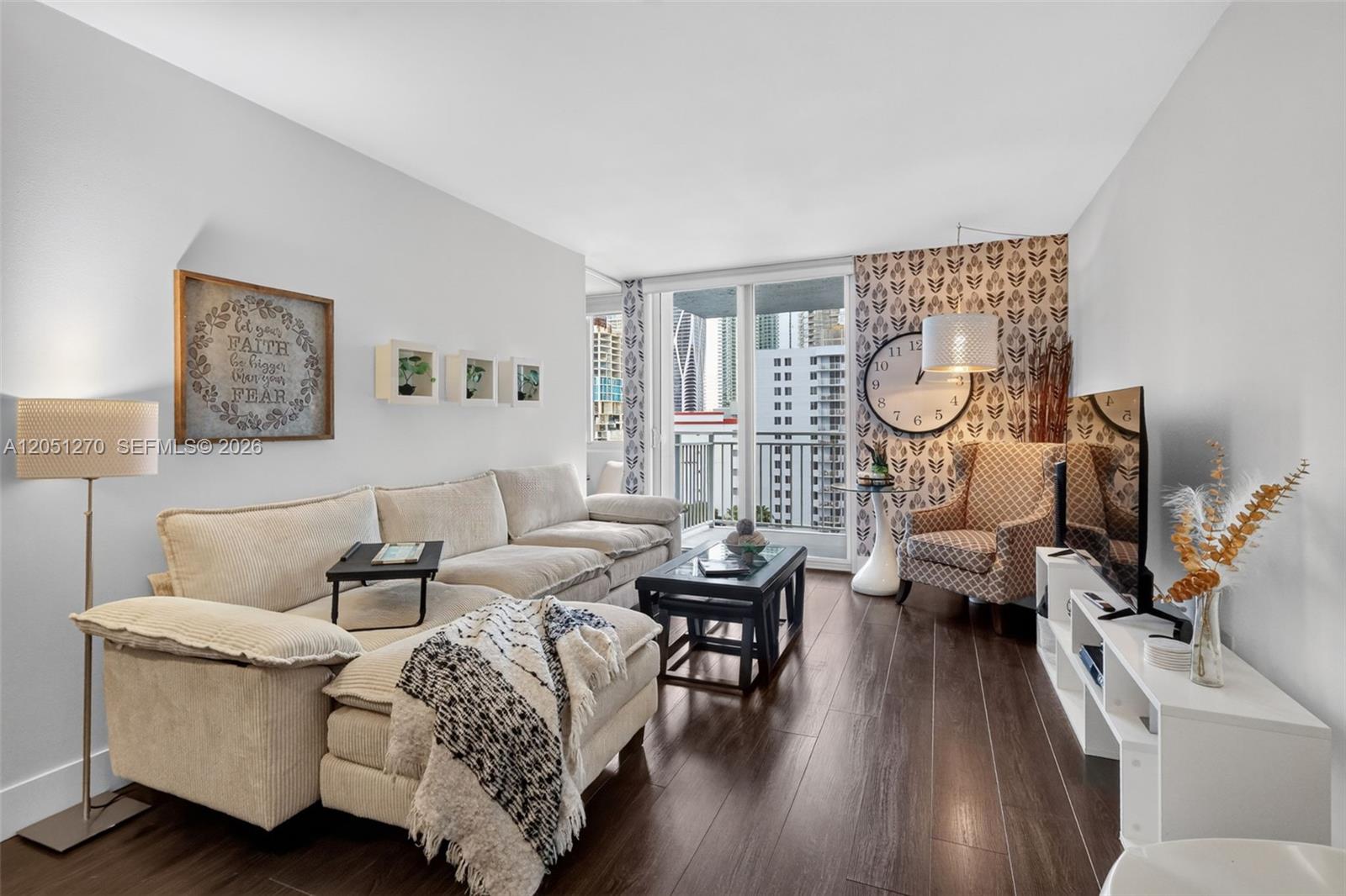 A living room features a sectional sofa, patterned wallpaper, a large wall clock, and balcony access — 850 N Miami Ave # 1202, Miami FL 33136, MIAMI, FL