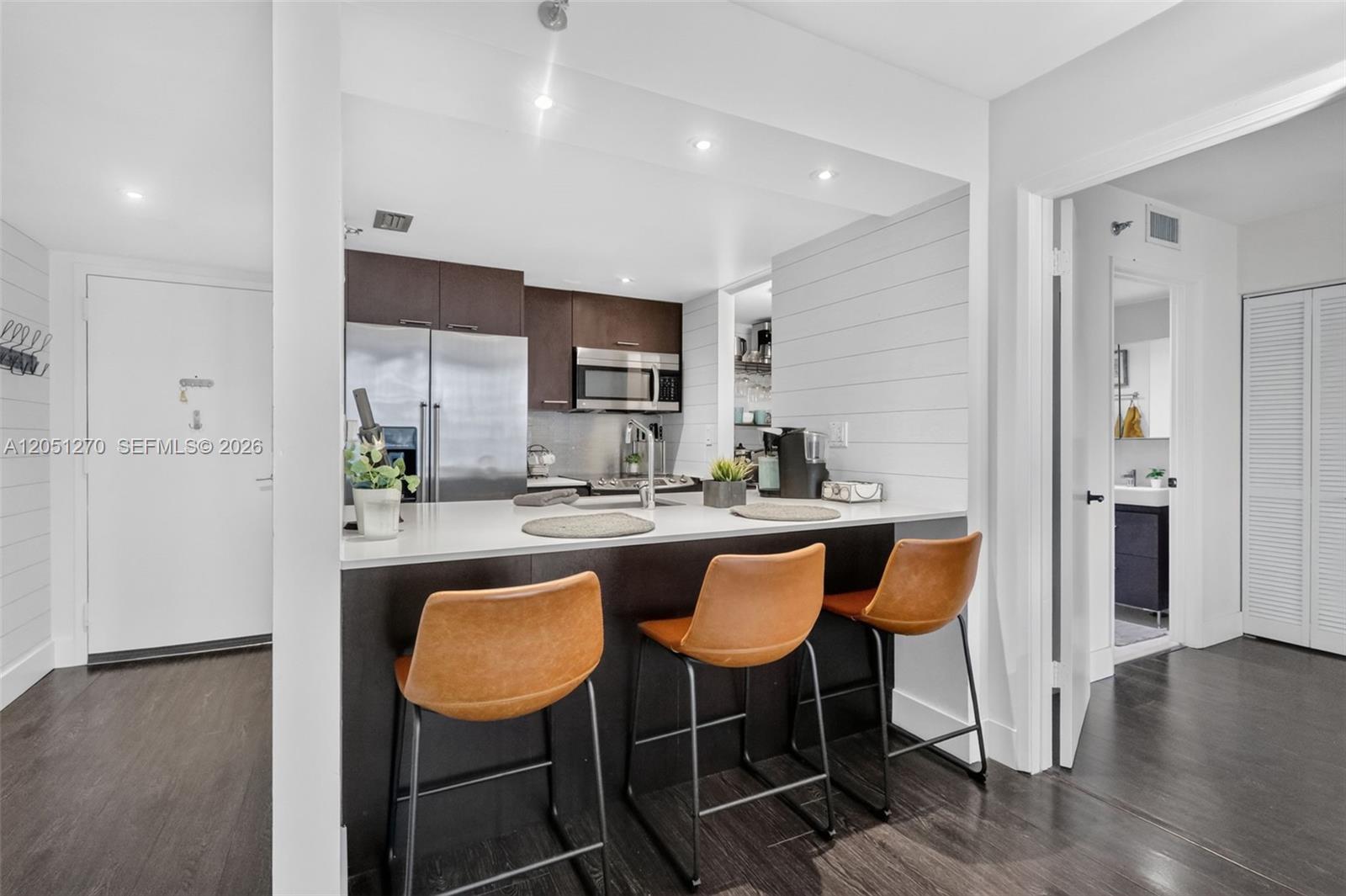 A kitchen with dark cabinets, stainless steel appliances, and a breakfast bar with three stools — 850 N Miami Ave # 1202, Miami FL 33136, MIAMI, FL