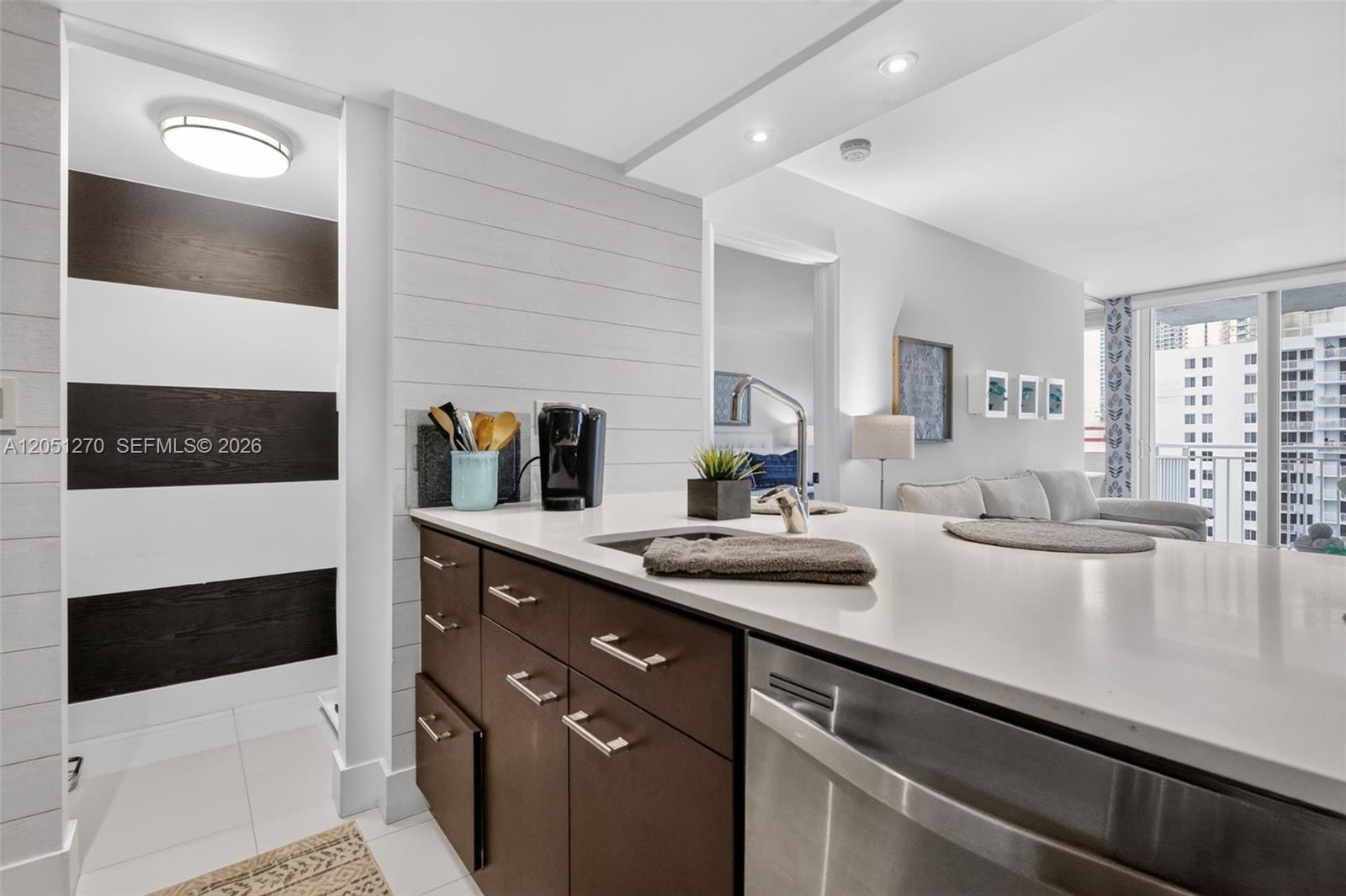 A kitchen island with dark cabinets and a white countertop sits before a living area — 850 N Miami Ave # 1202, Miami FL 33136, MIAMI, FL