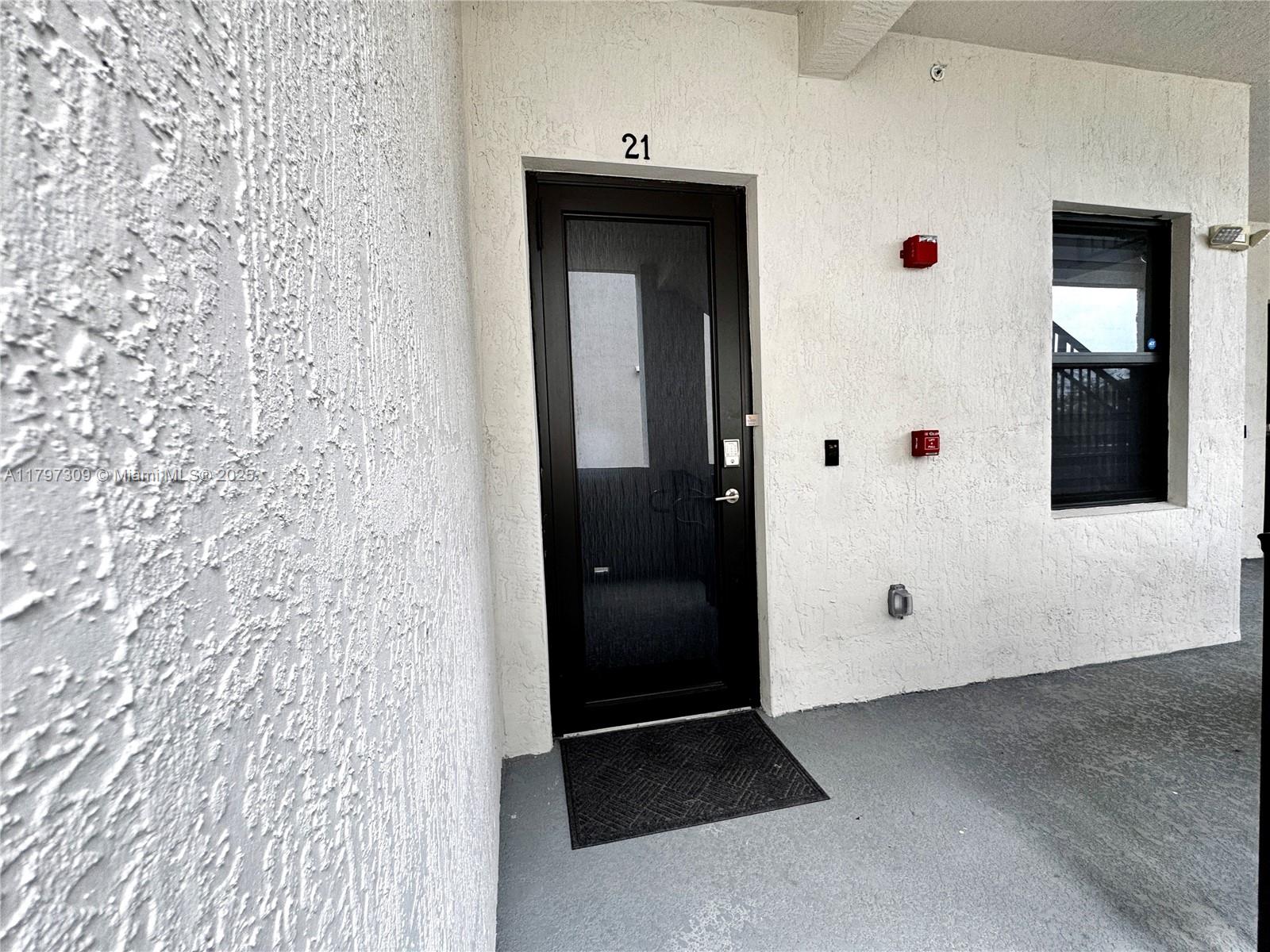 A black front door labeled 21 is set in a white stucco wall with a window — 8175 NW 104th Ave # 21, Doral FL 33178, DORAL, FL