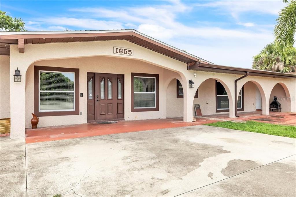 A single-story house features a concrete driveway, a covered porch with arches, and brown trim — 1655 DANIELS DRIVE, NORTH FORT MYERS, FL