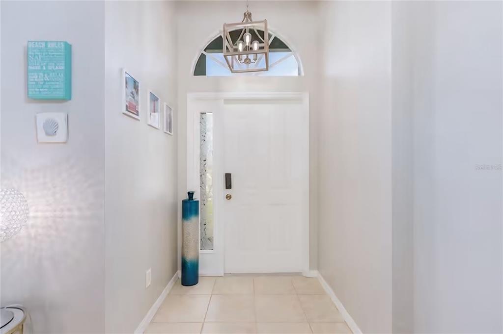 A bright entryway features a white front door, a tall blue vase, and a chandelier — 2705 SW 11TH PLACE, CAPE CORAL, FL