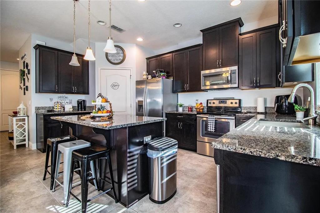 A kitchen features dark wood cabinets, granite countertops, a center island with stools, and appliances — 13886 ARCLID STREET, ORLANDO, FL