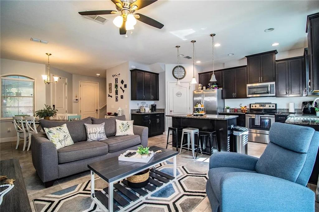 An open-concept living room and kitchen featuring dark cabinets, stainless appliances, and a gray sofa — 13886 ARCLID STREET, ORLANDO, FL
