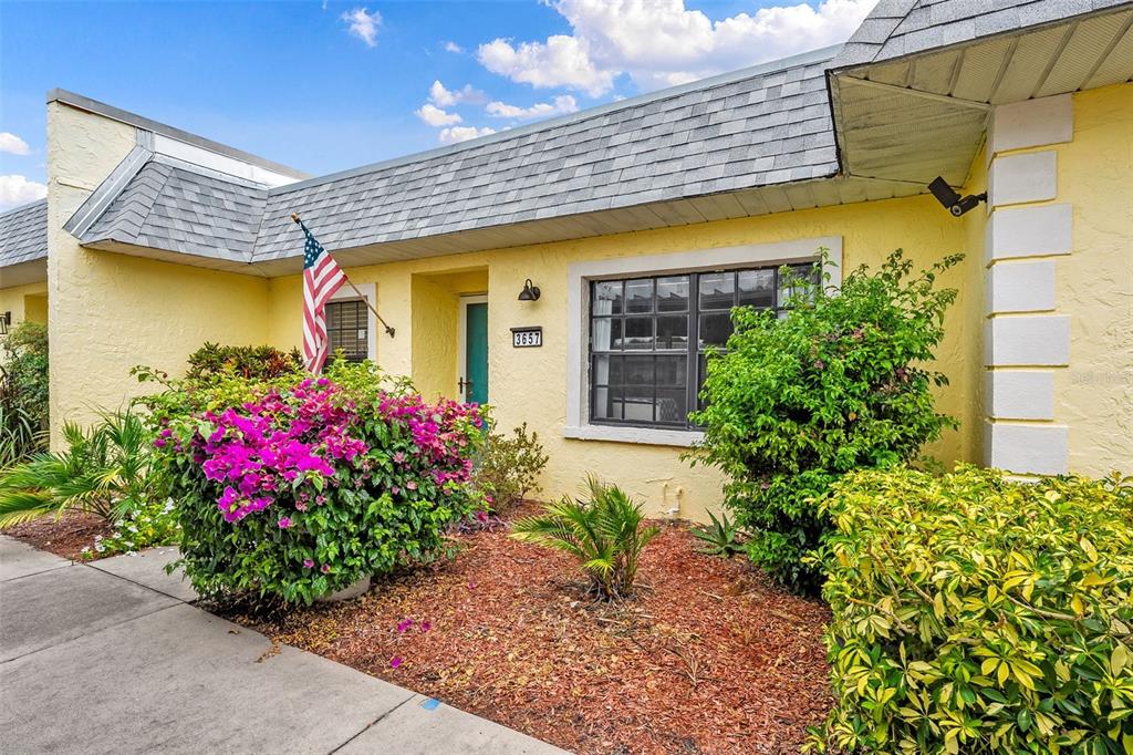 A yellow single-story home exterior features a gray shingled roof, a front door, and landscaping — 3657 TROPHY BOULEVARD, NEW PORT RICHEY, FL