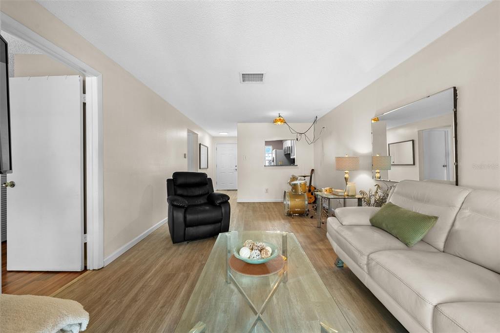 A living room features light wood-look flooring, a white sofa, a black recliner, and drums — 3657 TROPHY BOULEVARD, NEW PORT RICHEY, FL