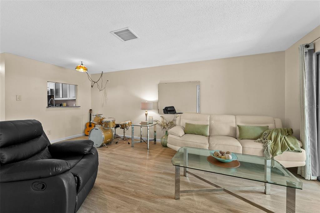 A living room features a beige sofa, a black recliner, a glass coffee table, and drums — 3657 TROPHY BOULEVARD, NEW PORT RICHEY, FL