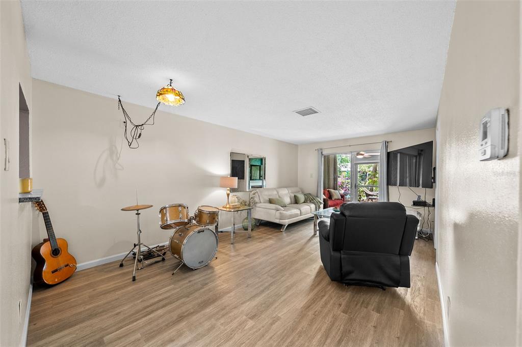 A living room with wood-look flooring, a drum set, a guitar, and a black recliner — 3657 TROPHY BOULEVARD, NEW PORT RICHEY, FL