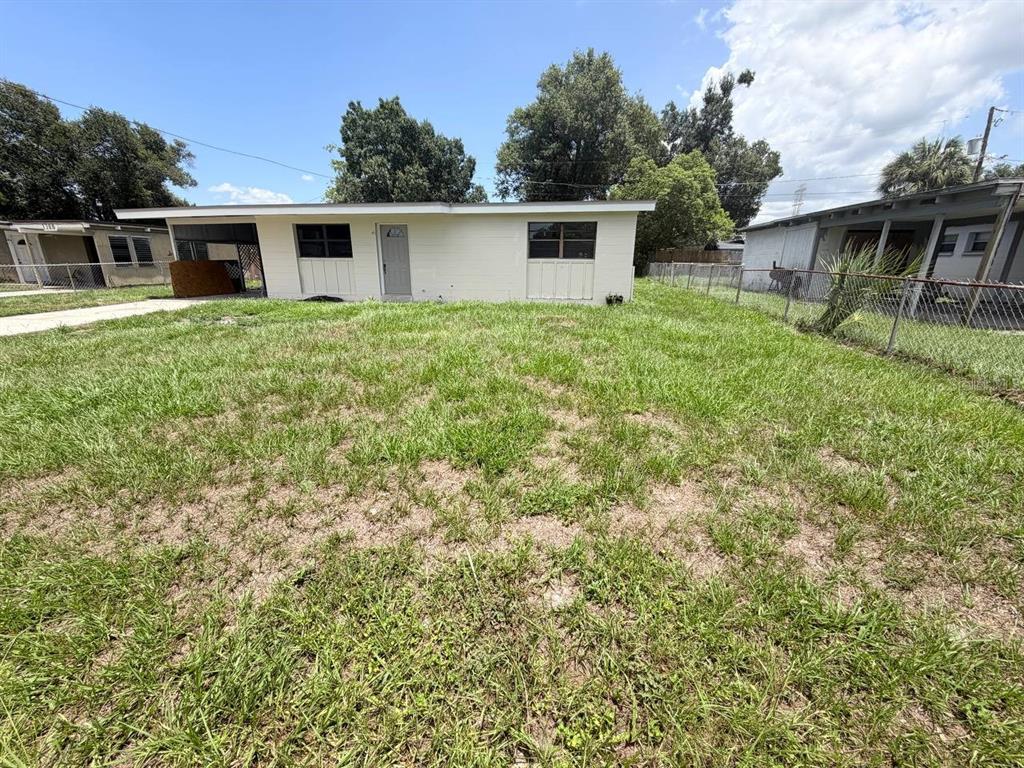 A single-story, light-colored house with a flat roof and a carport sits on a grassy lot — 1310 WARRINGTON WAY, TAMPA, FL