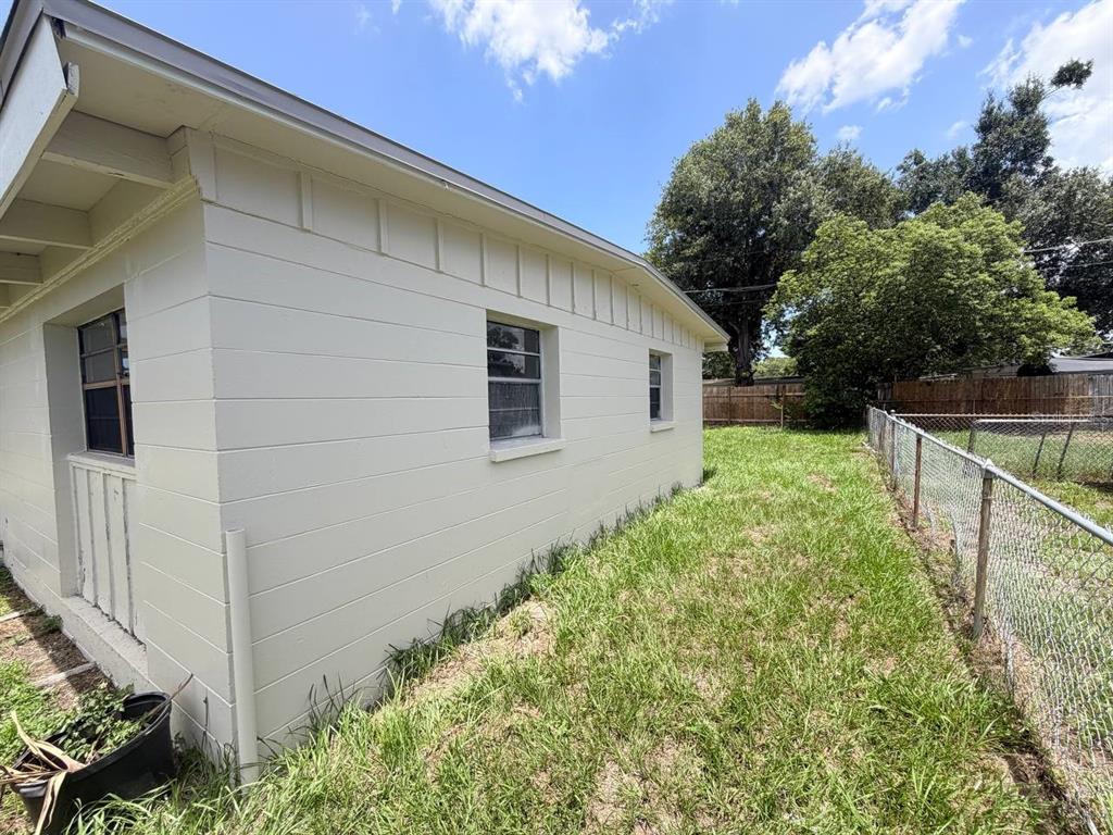 The exterior of a light-colored house features horizontal siding, two windows, and a chain-link fence — 1310 WARRINGTON WAY, TAMPA, FL