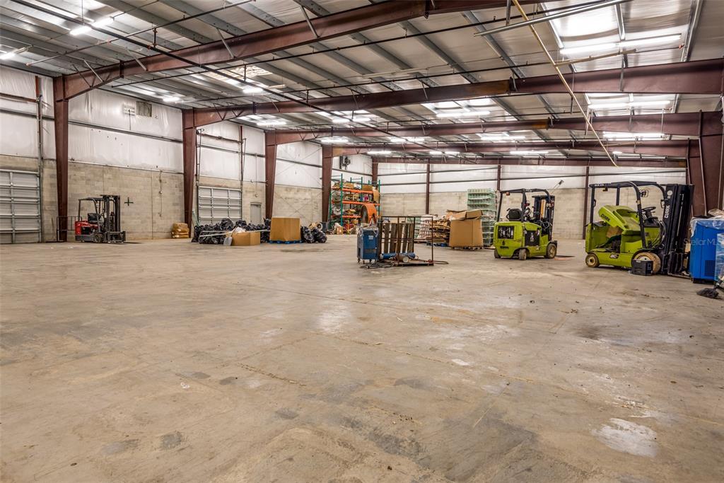 An industrial warehouse interior features a concrete floor, exposed steel beams, and several parked forklifts — 1780 BUSINESS CENTER LANE, KISSIMMEE, FL