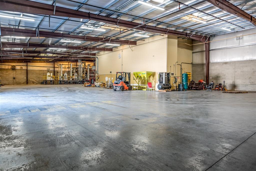 A large, open industrial warehouse space features a concrete floor, exposed steel beams, and equipment — 1780 BUSINESS CENTER LANE, KISSIMMEE, FL