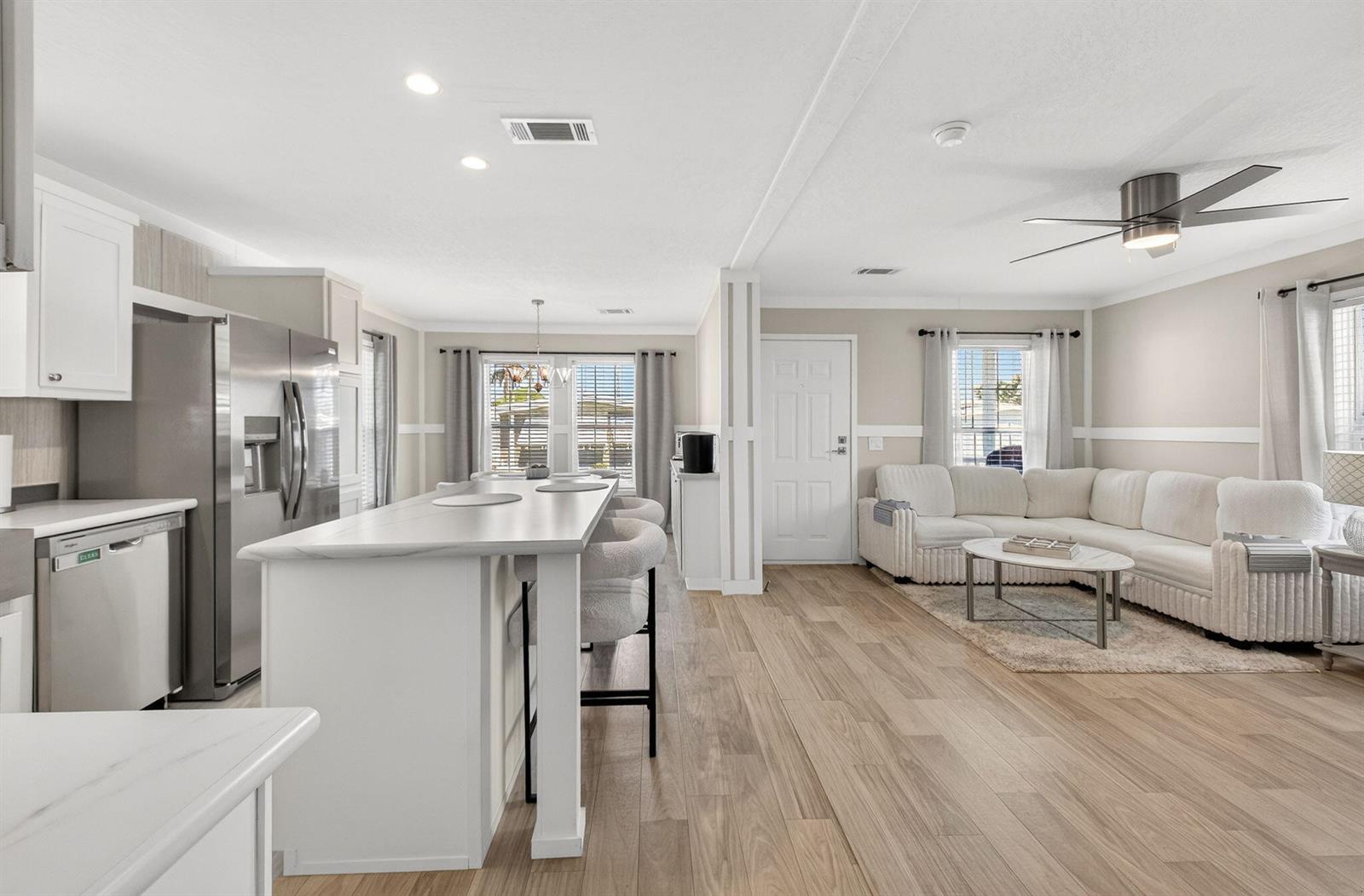 An open-concept kitchen and living area featuring white cabinetry, a marble island, and wood flooring — 58012 Bahama Bay, Boynton Beach FL 33436, BOYNTON BEACH, FL