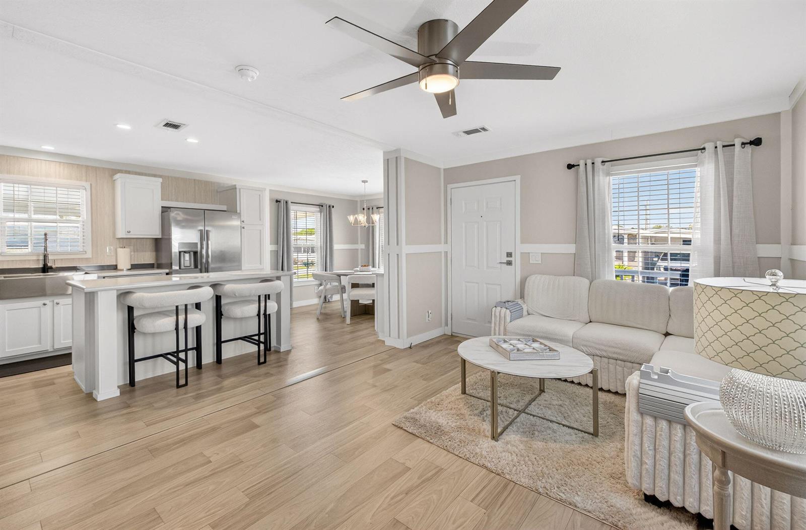 An open-concept living room and kitchen feature light wood flooring, white cabinetry, and neutral furniture — 58012 Bahama Bay, Boynton Beach FL 33436, BOYNTON BEACH, FL