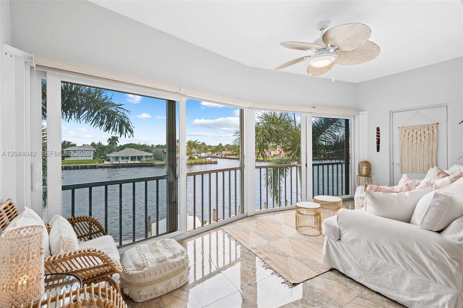 A sunlit living room features large sliding glass doors overlooking a canal and palm trees — 711 N Riverside Dr # 302, Pompano Beach FL 33062, POMPANO BEACH, FL