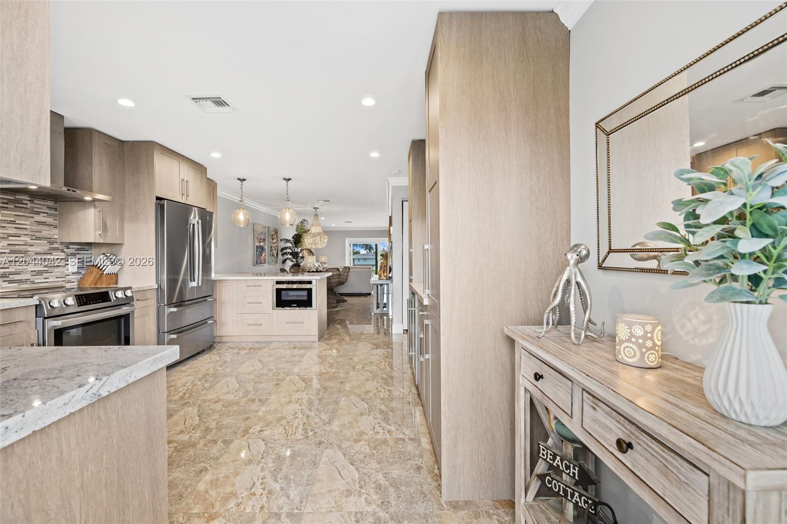 A modern kitchen features light wood cabinetry, stainless steel appliances, and polished marble flooring — 711 N Riverside Dr # 302, Pompano Beach FL 33062, POMPANO BEACH, FL