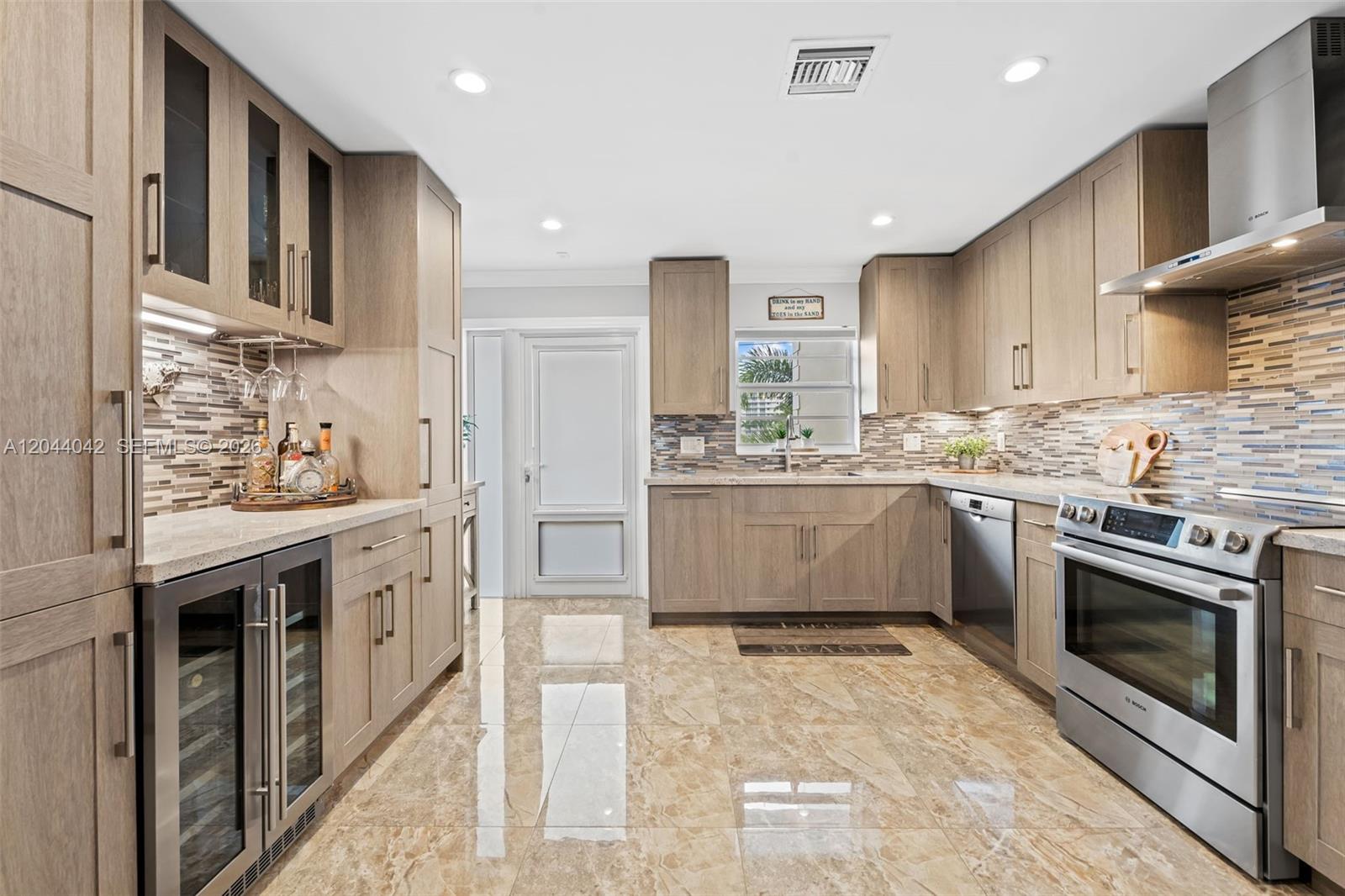 A modern kitchen features light wood cabinets, stainless steel appliances, and polished marble-look tile flooring — 711 N Riverside Dr # 302, Pompano Beach FL 33062, POMPANO BEACH, FL