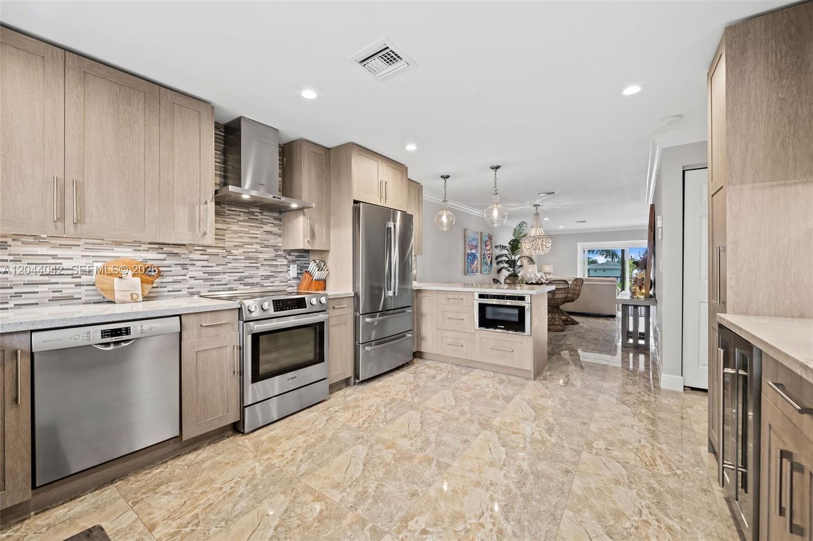 A modern kitchen features light wood cabinetry, stainless steel appliances, and polished marble flooring — 711 N Riverside Dr # 302, Pompano Beach FL 33062, POMPANO BEACH, FL