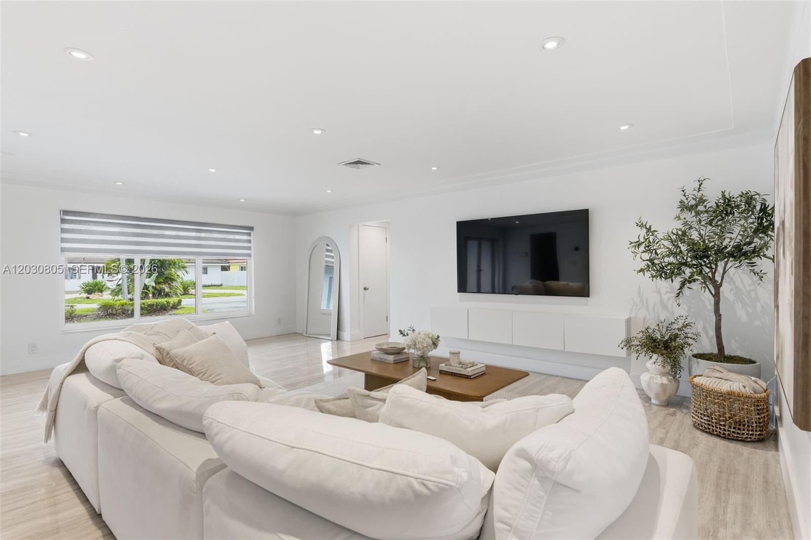 A bright living room features a white sectional sofa, a wall-mounted television, and light flooring — 19040 S Saint Andrews Dr, Hialeah FL 33015, HIALEAH, FL