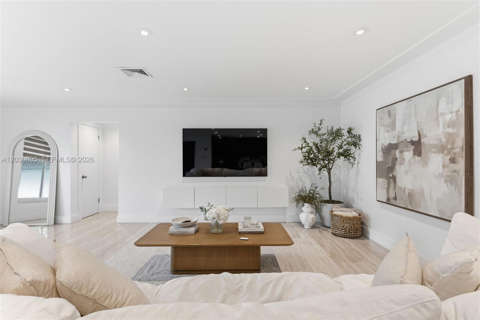 A bright living room features a wall-mounted television, a wooden coffee table, and white furniture — 19040 S Saint Andrews Dr, Hialeah FL 33015, HIALEAH, FL