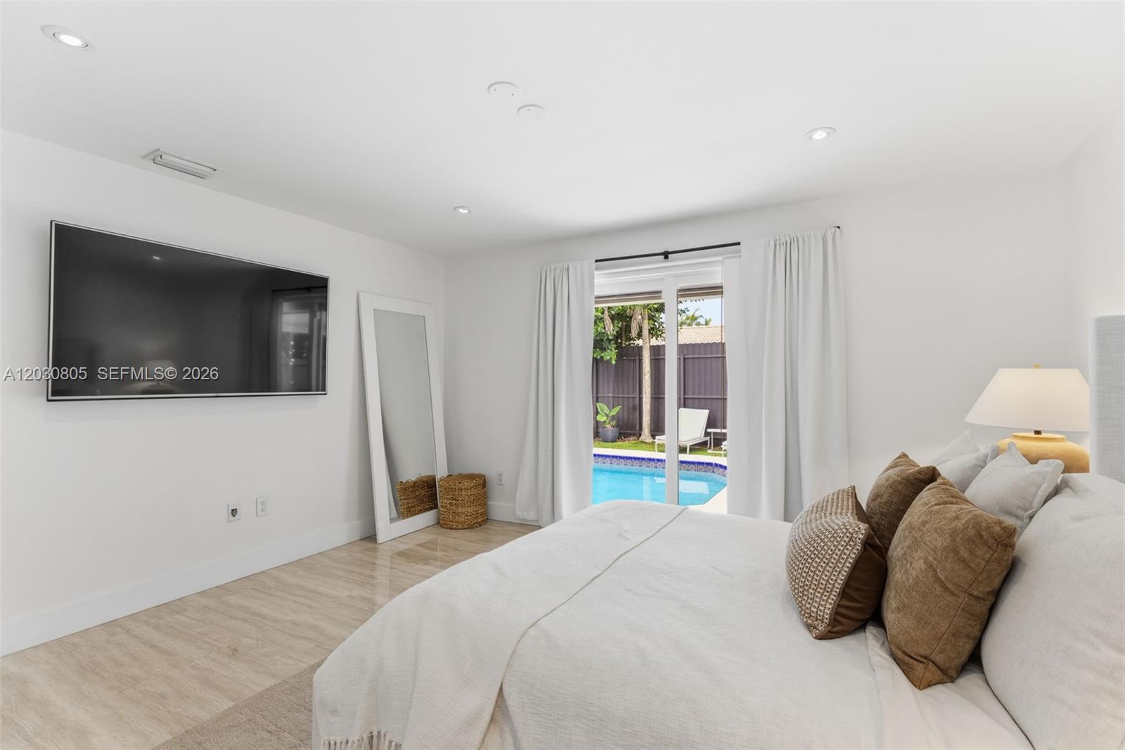 A bedroom features a wall-mounted television, a floor mirror, and sliding doors overlooking a pool — 19040 S Saint Andrews Dr, Hialeah FL 33015, HIALEAH, FL