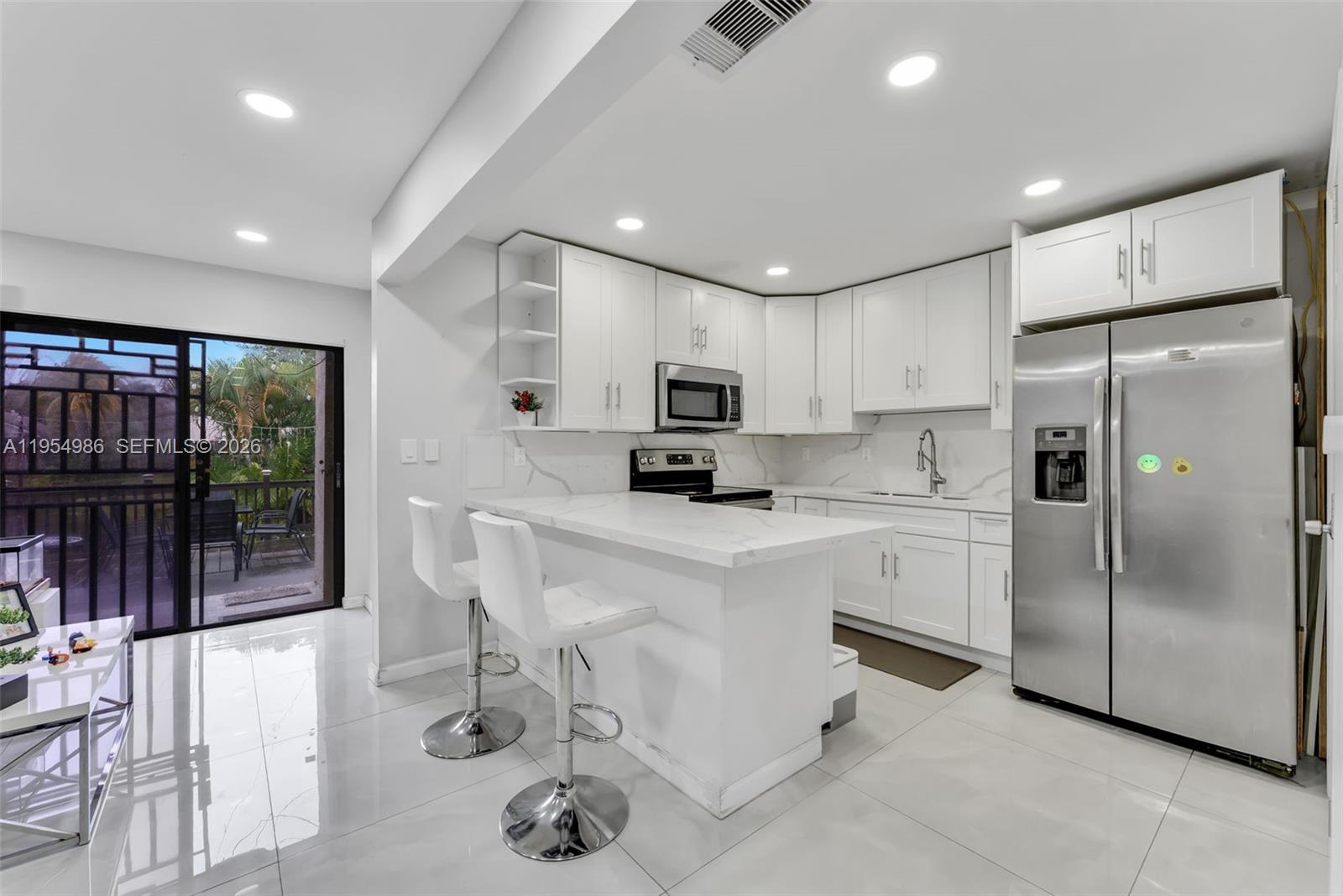 A modern white kitchen features a marble-topped breakfast bar, stainless steel appliances, and tile flooring — 12233 SW 24th Ter # 35, Miami FL 33175, MIAMI, FL