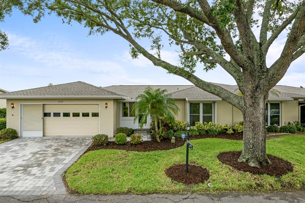 A single-story house with a beige exterior, a paved driveway, and a large oak tree — 2703 LANCASTER DRIVE, SUN CITY CENTER, FL