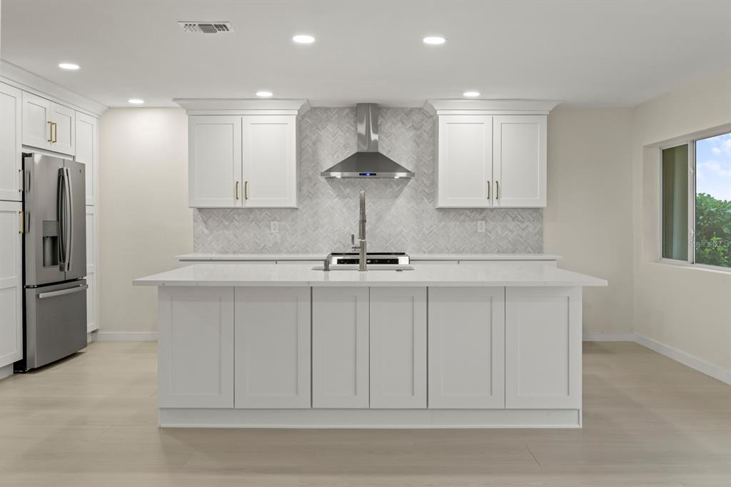 A modern kitchen features white cabinetry, a large central island, and a herringbone tile backsplash — 2703 LANCASTER DRIVE, SUN CITY CENTER, FL