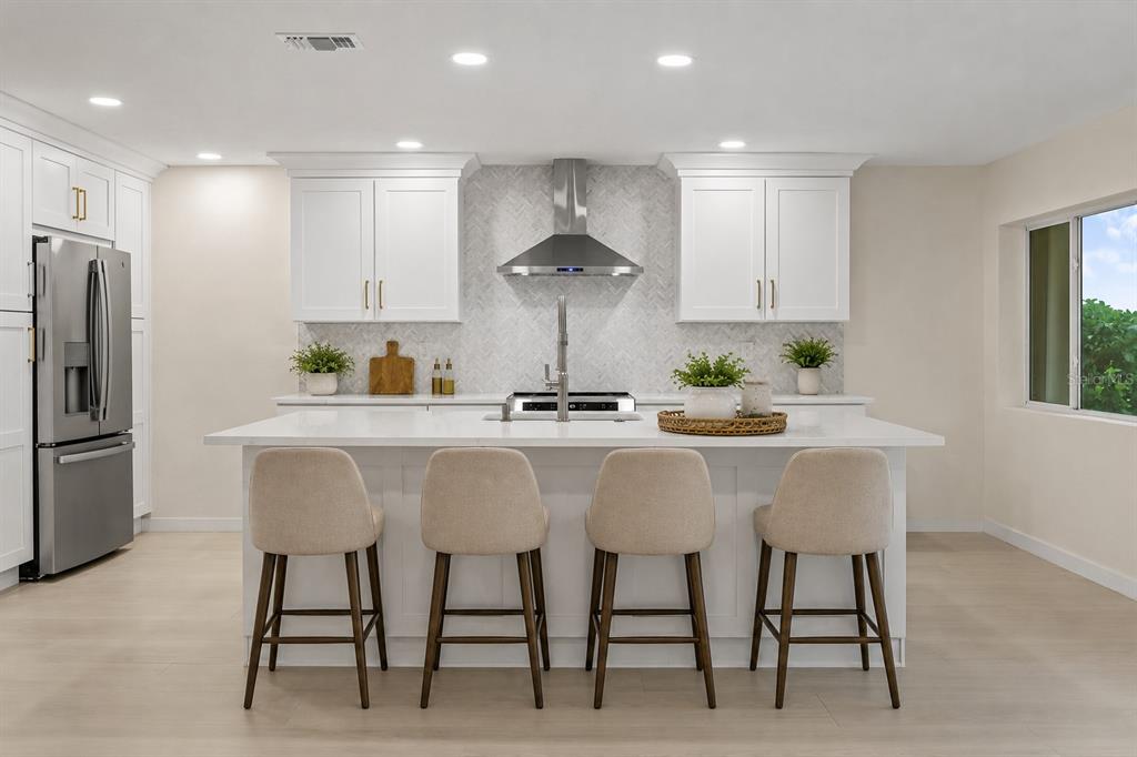 A modern kitchen features white cabinetry, a central island with four stools, and stainless appliances — 2703 LANCASTER DRIVE, SUN CITY CENTER, FL