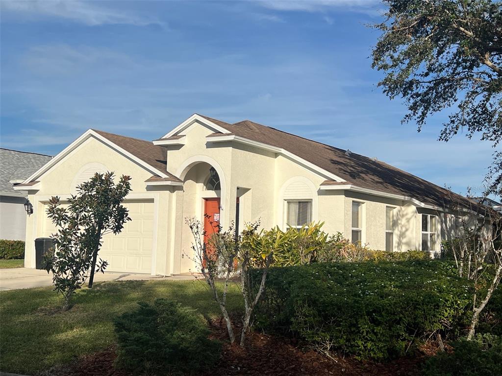 A single-story house with a tan stucco exterior, a brown roof, and a red front door — 6227 YELLOWTOP DRIVE, LAKEWOOD RANCH, FL
