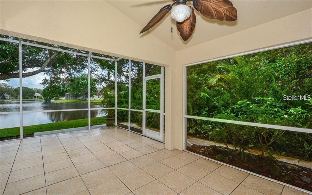 A screened-in porch with tile flooring, a ceiling fan, and views of a pond — 6227 YELLOWTOP DRIVE, LAKEWOOD RANCH, FL