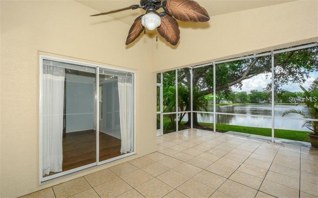 A screened-in patio with tile flooring, a ceiling fan, and a view of a lake — 6227 YELLOWTOP DRIVE, LAKEWOOD RANCH, FL