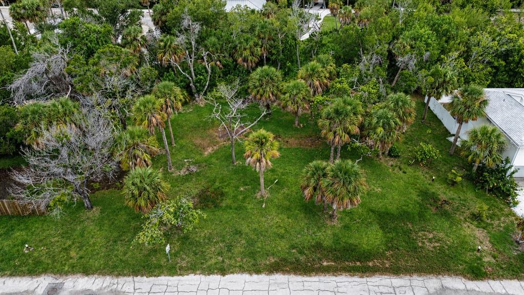 An aerial view shows a grassy, tree-filled vacant lot bordered by a road and houses — 561 GULF BAY ROAD, LONGBOAT KEY, FL