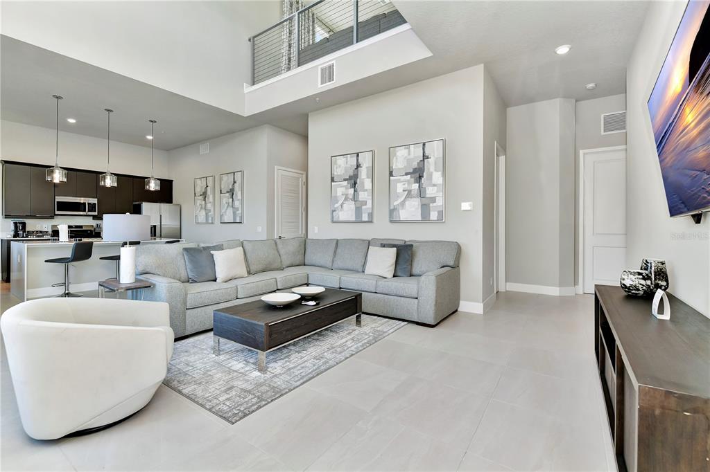 A modern living room with a sectional sofa, coffee table, and open kitchen area — 7740 SANDY RIDGE DRIVE UNIT 231, KISSIMMEE, FL