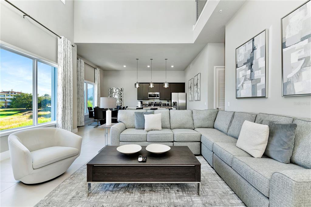 A modern living room with a sectional sofa, coffee table, and open kitchen in background — 7740 SANDY RIDGE DRIVE UNIT 231, KISSIMMEE, FL
