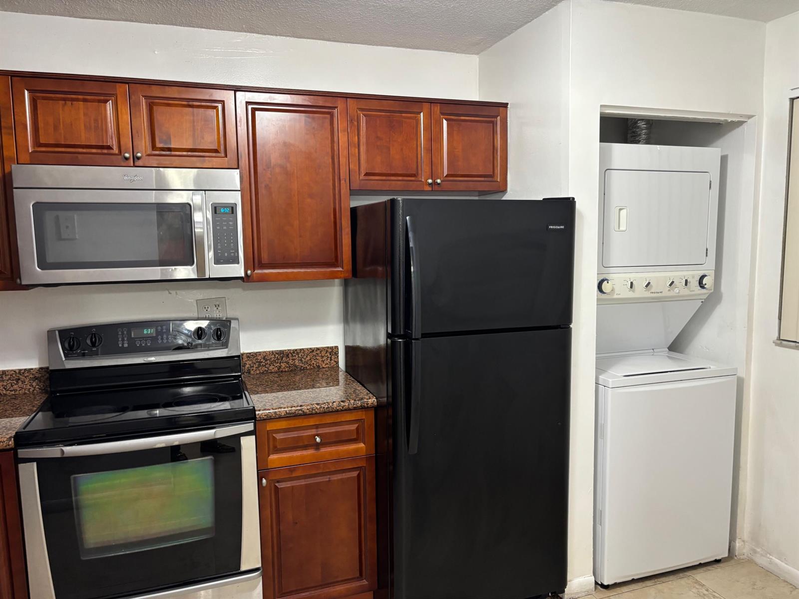 A kitchen featuring wood cabinets, stainless steel microwave, black appliances, and a stacked laundry unit — 9959 Nob Hill Place, Sunrise FL 33351, SUNRISE, FL