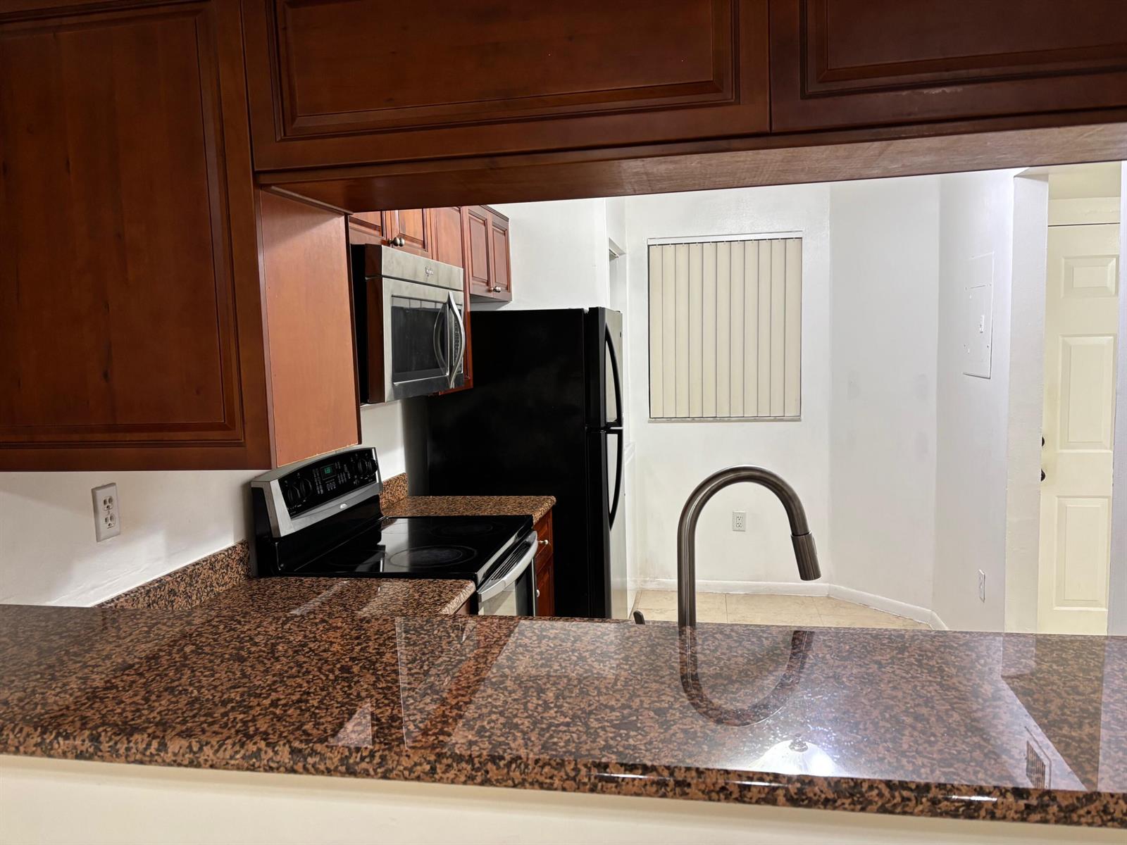 A kitchen features dark wood cabinets, granite countertops, and black appliances — 9959 Nob Hill Place, Sunrise FL 33351, SUNRISE, FL