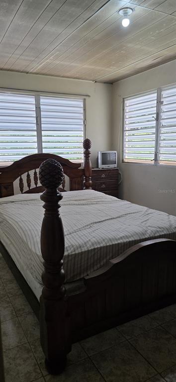 A bedroom features a wooden four-poster bed, tiled floors, and two windows with louvered blinds — 53 Aquilino CARR. 430, BO. OVEJAS, ANASCO, PR